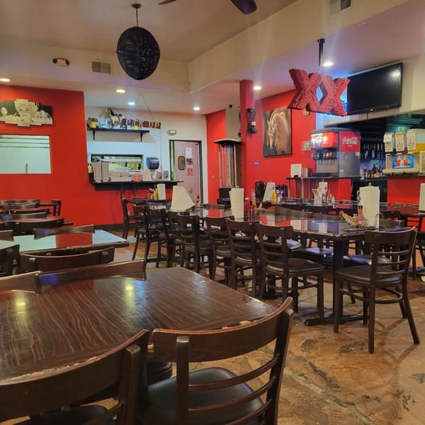 Interior of Lil Alex BBQ with red walls, dark tables, chairs, and a drink station.