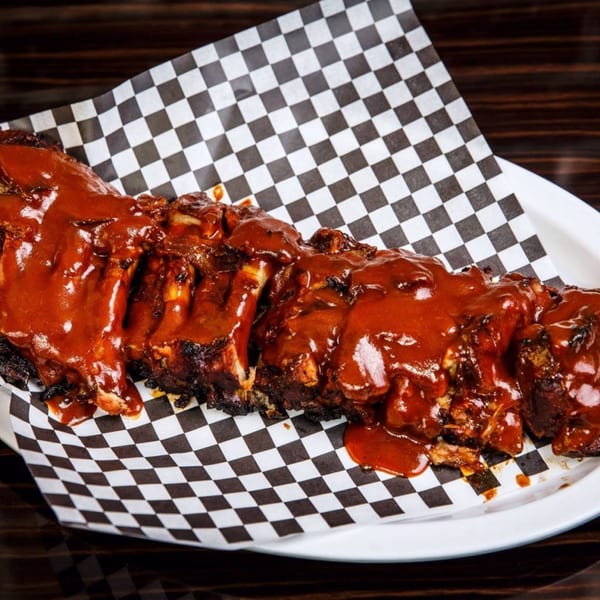 A rack of Lil Alex BBQ ribs covered in rich, red barbecue sauce on checkered paper.