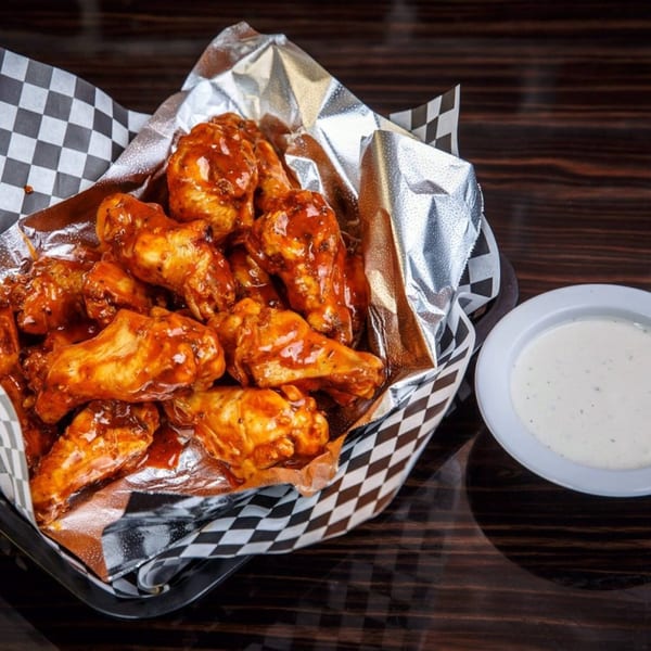 A basket of Lil Alex BBQ's saucy chicken wings with a side of ranch dressing.